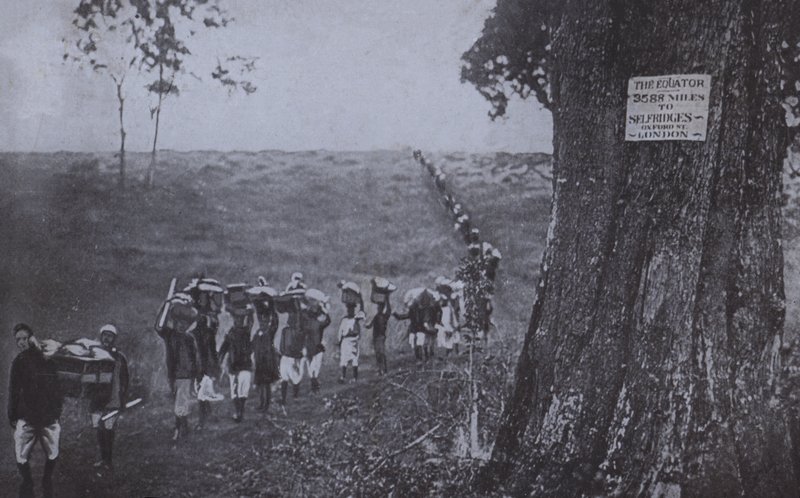 Line of men carrying goods from the equator to Selfridges, London by English Photographer