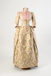 Dress of light brown silk woven with a design of mauve, blue and yellow flowers and green leaves, light pink ribbed silk bodice panel and cuffs