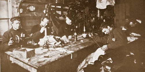 In the Hut during mid-winter, the men engaged in sewing furs for clothing to be used in springtime sledging, published London 1907