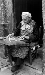 Lacemaker, an elder woman, in Bruges is seated at her doorway while making lace