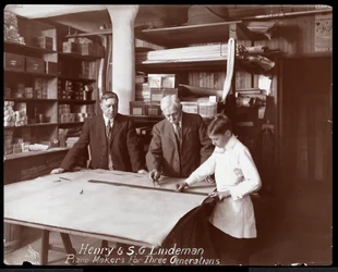 Portrait of Henry and S.G. Lindeman with their son or grandson standing over shop drawings for a piano, 1910