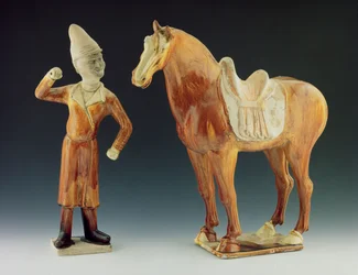 Groom figure wearing a coat and peaked hat with a saddled horse, Tang Dynasty