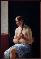 Nude Model Sitting. Portrait of a Woman Braiding Her Hair