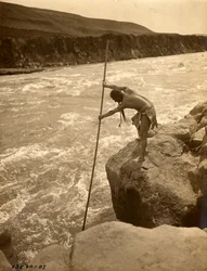 Tlakluit Indian, standing on rock, fishing with dip net