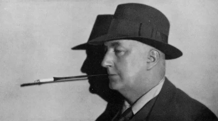 Portrait of Edgar Wallace, wearing hat and smoking cigarette in holder