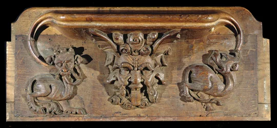 A misericord depicting three human faces flanked by monsters, New College Chapel, Oxford, late 14th century
