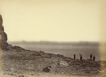 View of shore with ships on horizon and five figures standing on beach