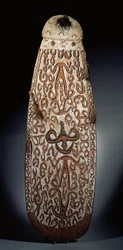 Oval Asmat shield, carved in relief with scrolling ornament incorporating highly stylised figures, plaited tassels to the border