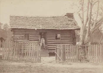 Albumen print of a woman and two children in front of a log house in Georgia