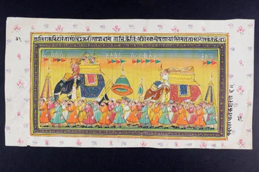 Dignitaries ride on the back of an elephant in a howdah attended by a mahout or elephant driver