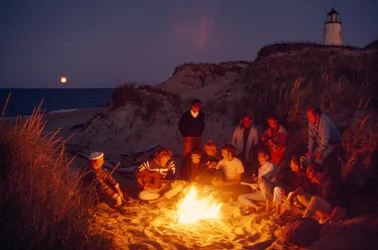 Friends gather around a summer campfire at Great Point Lighthouse. Nantucket Island