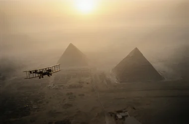 The vintage airplane Vimy flies above fog-shrouded pyramids during a golden sunrise