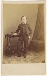 Unidentified little boy in suit standing at a table with books on top