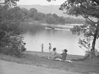 A family enjoying themselves next to a lake, boat on lake, hills in background