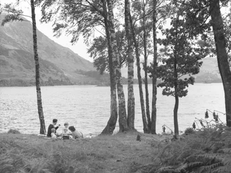 A family relaxing near to lake with trees to right and hills in background