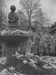 Children placing bunches of daffodils on fountain with statue on top