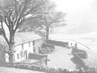 Farmer with lamb under arm and dog driving sheep through gate into farmyard with another farmer waiting