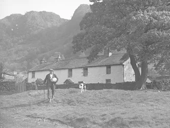 Farmer with lamb under arm and dog following