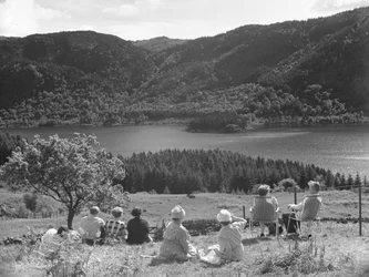 Group of people sitting on grass or deck chairs looking at a view of Thirlmere