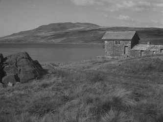 Rocks in foreground on left and building on right with Devoke Water beyond