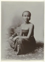 Studio portrait of a seated young Javanese woman in a sarong with batik motif