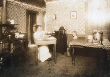 Woman inserting bristles into tooth brushes in her kitchen, c.1912