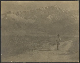 Woman Walking on Path Towards Mountains