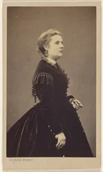 Unidentified woman wearing a dark dress, standing, in profile
