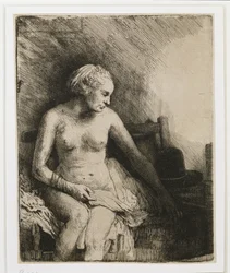 A woman at the bath with a hat beside her