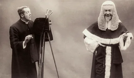 A man in a cassock aims the lens of his camera at a man dressed like a pope