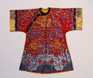A semi formal robe of red satin embroidered in silks and gilt thread with dragons amidst scrolling clouds above a turbulent sea wave border