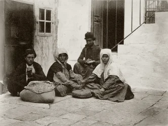 Women grinding flour with round millstones within a courtyard of a house in Jerusalem