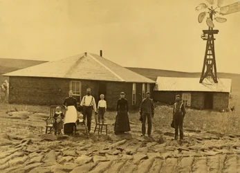 Family of homesteaders outside their sod house, with a windmill on the roof of the adjoining building, in Custer County, Nebraska, c. 1885