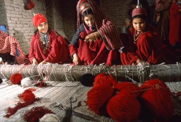 Turkoman tribeswomen weavers trim knots in the warp of a rug on a loom in a village