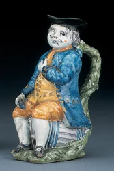 Toby jug with pale manganese face and hands, holding an empty globular buff-coloured jug in washed blue jacket and breeches, and green waistcoat, c.1800