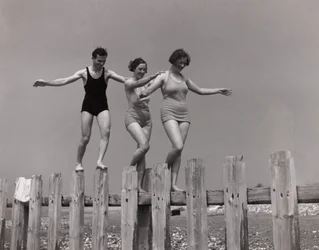 Two women and a man walking along a groyne, c 1930s