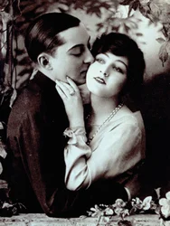Half-Length Portrait of a Young Couple Leaning Against a Balcony Decorated with Plants. The Man Has His Arm Around the Girl