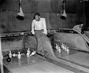 African-American man attending ten pins at bowling alley, to manually reset the pins