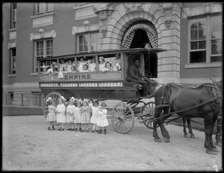 Small Girls Pose in and in Front of a Horse-Drawn Wagon, in Front of an Unidentified Building, Probably the Roman Catholic Orphan Asylum, Kingsbridge, Bronx, c.1910