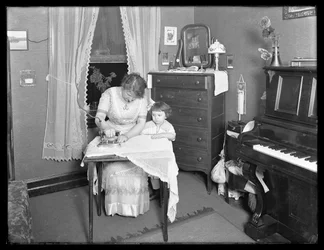 Unidentified woman demonstrating the use of an electric iron, watched by little girl, c.1913-14