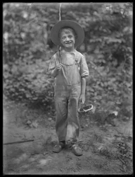 William Gray Hassler in straw hat and overalls, carrying fishing pole and basket in the woods